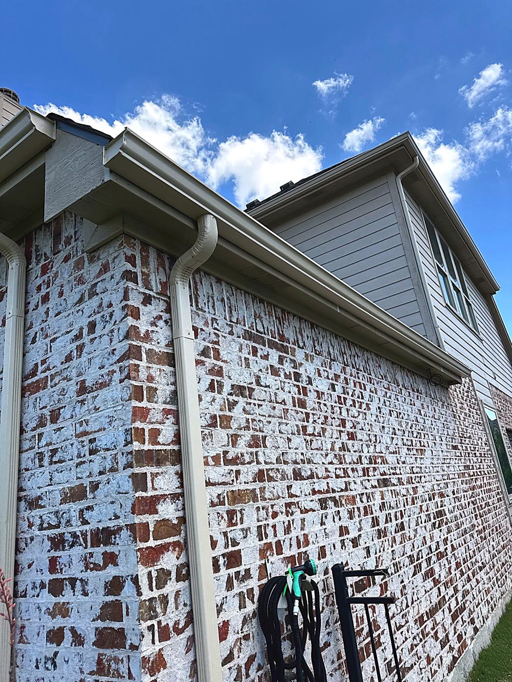 New seamless gutters and a clean roofline on a whitewashed brick home exterior in the Garland area